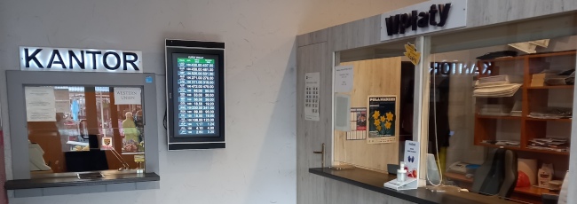 Zdjęcie lokalu firmy pokazujące od lewej do prawej: okno kantoru i wpłat międzynarodowych przy którym po prawej jest monitor z kursami walut, a następnie dwa stanowiska obsługi